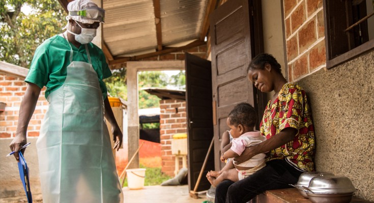 A woman sits with her small child awaiting treatment for monkeypox at a facility run by Doctors Without Borders in the Central African Republic. There is a medical professional speaking to them wearing PPE and carrying a clipboard 