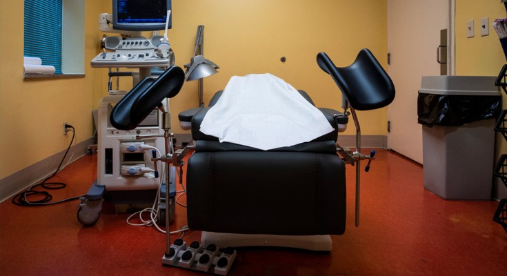 A black examination table stands in the middle of an empty room, surrounded by medical equipment