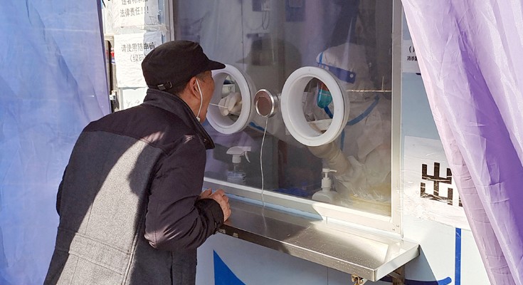 A person in protective gear inside a kiosk swabs the mouth of a customer.