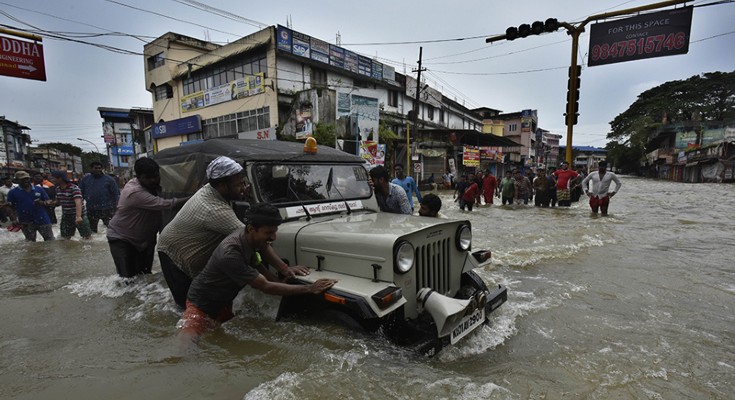 People push vehicles stuck in the flood water at Panadala in district Pathanamthitta, India