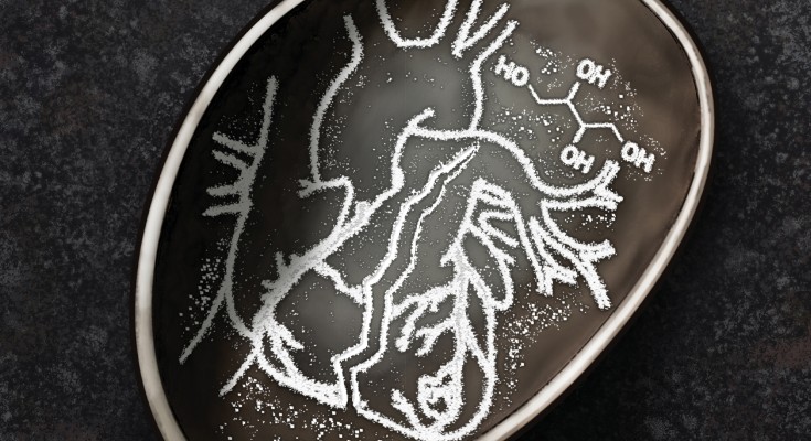A spoon contains a broken heart drawn with erythritol granules, representing the health effects of this food additive.