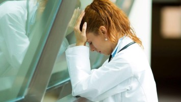 Junge Ärztin depressiv am Klinikfenster lehnend