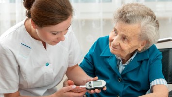 Pflegerin misst Blutzuckerspiegel einer Seniorin