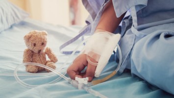 Kinderhand und Teddy im Klinikbett