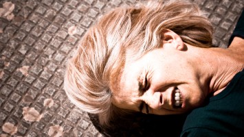Frau liegt mit verzerrtem Gesicht auf dem Boden