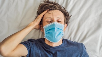 Ein Mann liegt erschöpft mit Maske im Bett