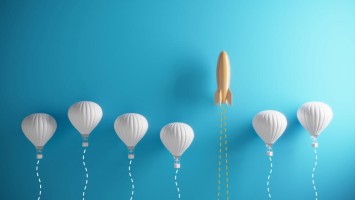 Mehrere weiße Ballons und eine Rakete steigen in den Himmel auf