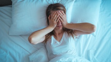 Junge Frau liegt im Bett und hält sich die Hände vors Gesicht