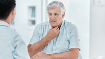 Älterer Patient sitzt mit Halsschmerzen beim Arzt