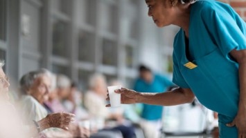 Pflegerin reicht Bewohnerin Wasser