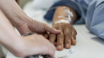 Ärztin hält Hand eines Patienten, der im Krankenbett liegt