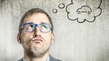 Mann mit blauer Brille denkt an ein Auto und schaut skeptisch