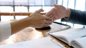 Handschlag von Frau und Mann vor juristischen Symbolen