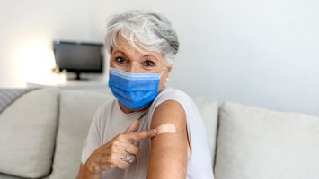 Frau mit Maske deutet auf ihren Arm