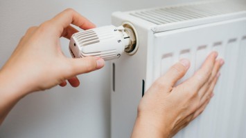 Hände bedienen Thermostat an Heizung und fühlen Wärme