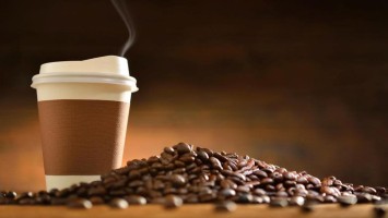 Kaffee im Einwegbecher mit verstreuten Kaffeebohnen