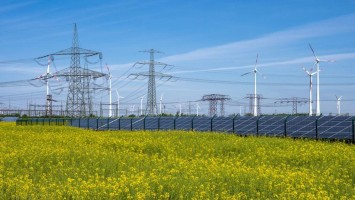 Strommasten, Windräder und Photovoltaik-Panels hinter Rapsfeld