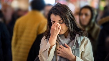 Frau steht in der Menge und hält die Hand vors Gesicht