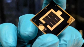 A hand in a light blue rubber glove is holding a solar cell.