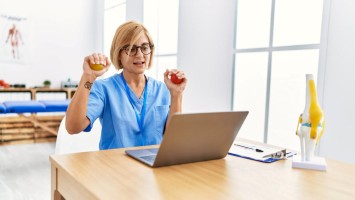 Physiotherapeutin hält Bälle in der Hand vor einem Laptop