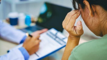 Frau sitzt besorgt beim Arzt und hält sich den Kopf