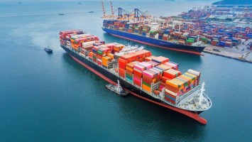 Zwei Frachtschiffe: eines verlässt den Hafen, das andere ist angedockt. 