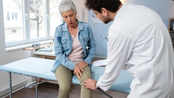 Arzt untersucht Knie einer Seniorin