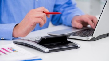Mann an Laptop mit Taschenrechner