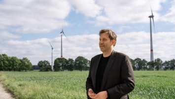 Bundesfinanzminister Klingbeil vor einem Acker, dahinter Windkraftanlagen