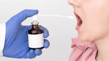 Ein Arzt sprüht ein antimikrobielles und entzündungshemmendes Spray in den entzündeten Hals eines Mädchens.