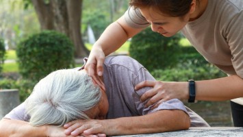 Ohnmächtige ältere Frau am Tisch und Helferin