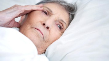 Ältere Frau mit Kopfschmerzen im Bett