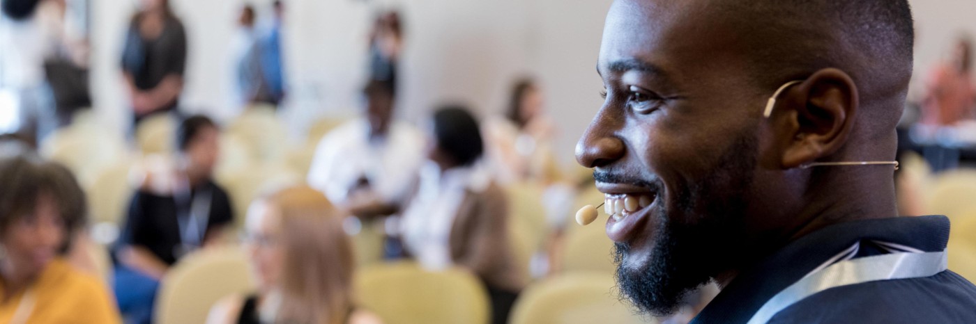 A middle-aged male speaker smiles at an unseen person as he prepares to address the Expo audience.