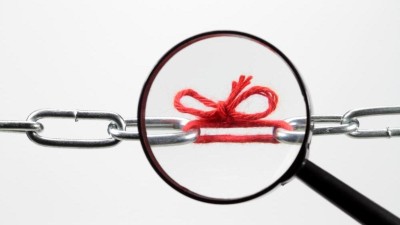 Lupe zeigt auf eine rote geknüpfte Stoffschleife in einer silbernen Gliederkette