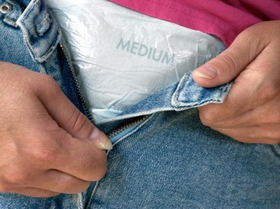Eine Frau schließt den Reißverschluss ihrer Jeans-Hose über einer Inkontinenz Windel (Symbolbild mit Model)