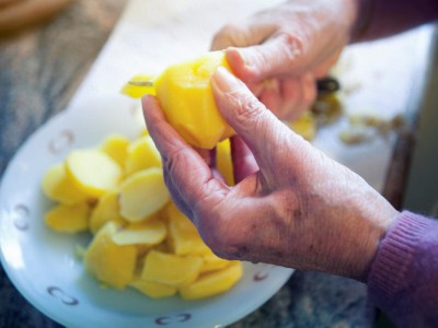 Hände einer alten Dame, die Kartoffeln schneidet