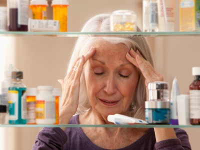 Frau mit Kopfschmerzen vor Medikamentenschrank