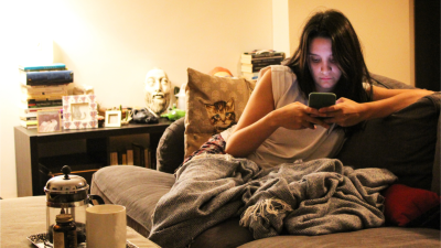 Frau sitzt auf dem Sofa mit Handy in der Hand