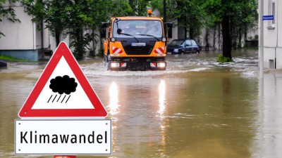 Straßenschild "Klimawandel" steht an einer überfluteten Straße
