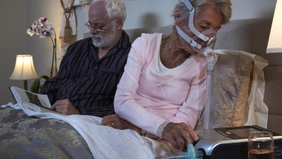Älteres Paar sitzt im Bett, Frau mit Beatmungsgerät
