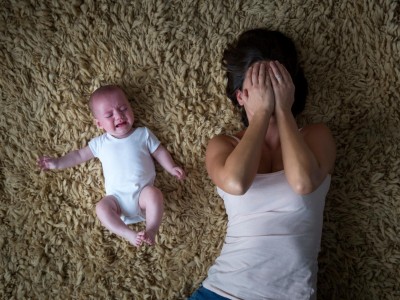 Frau verdeckt ihr Gesicht und liegt neben weinendem Baby