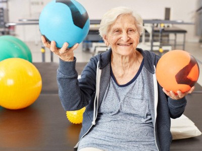 Alte Frau hält Sportbälle in Fitnessstudio hoch