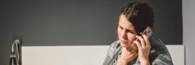 Eine kranke Frau sitzt im Bett und ruft ihre Arztpraxis an