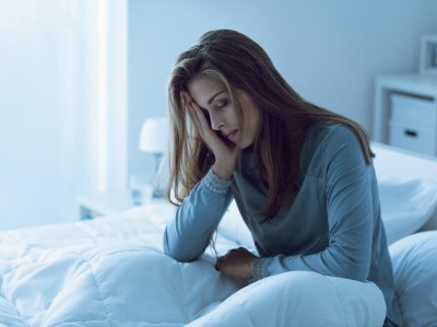 Eine Person sitzt müde im Bett und stützt den Kopf auf die Hände