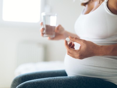 Schwangere Frau hält Tablette und Glas Wasser
