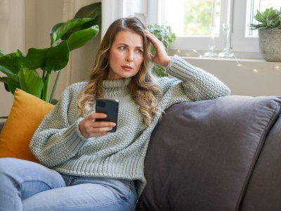 Eine junge Frau mit Smartphone in der Hand sitzt auf dem Sofa