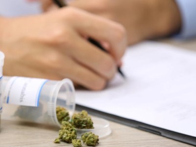 Arzt schreibt ein Rezept, daneben Dosen mit Cannabis