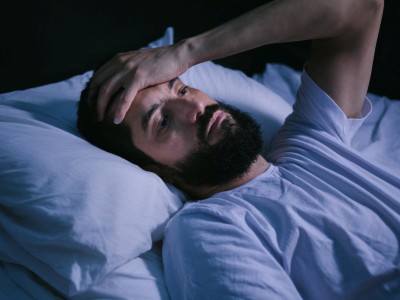 Junger bärtiger Mann liegt im Bett und hält sich die Stirn