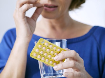 Frau hält Anti-Baby-Pille und Glas Wasser in der Hand