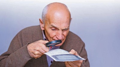 Älterer Herr mit Lupe untersucht Papier 